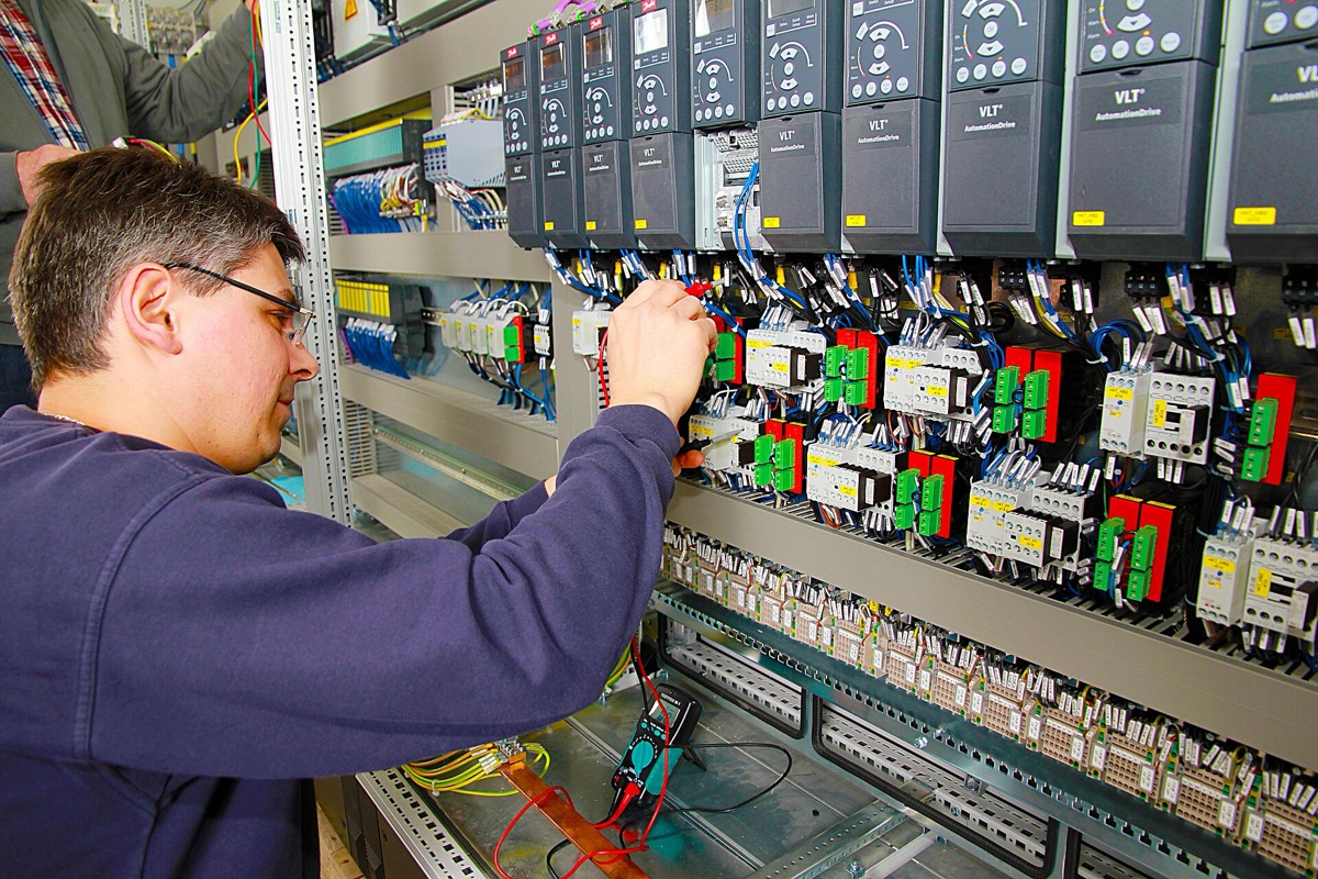 Elektryk wykonujący pomiary multimetrem w szafie sterowniczej automatyki przemysłowej